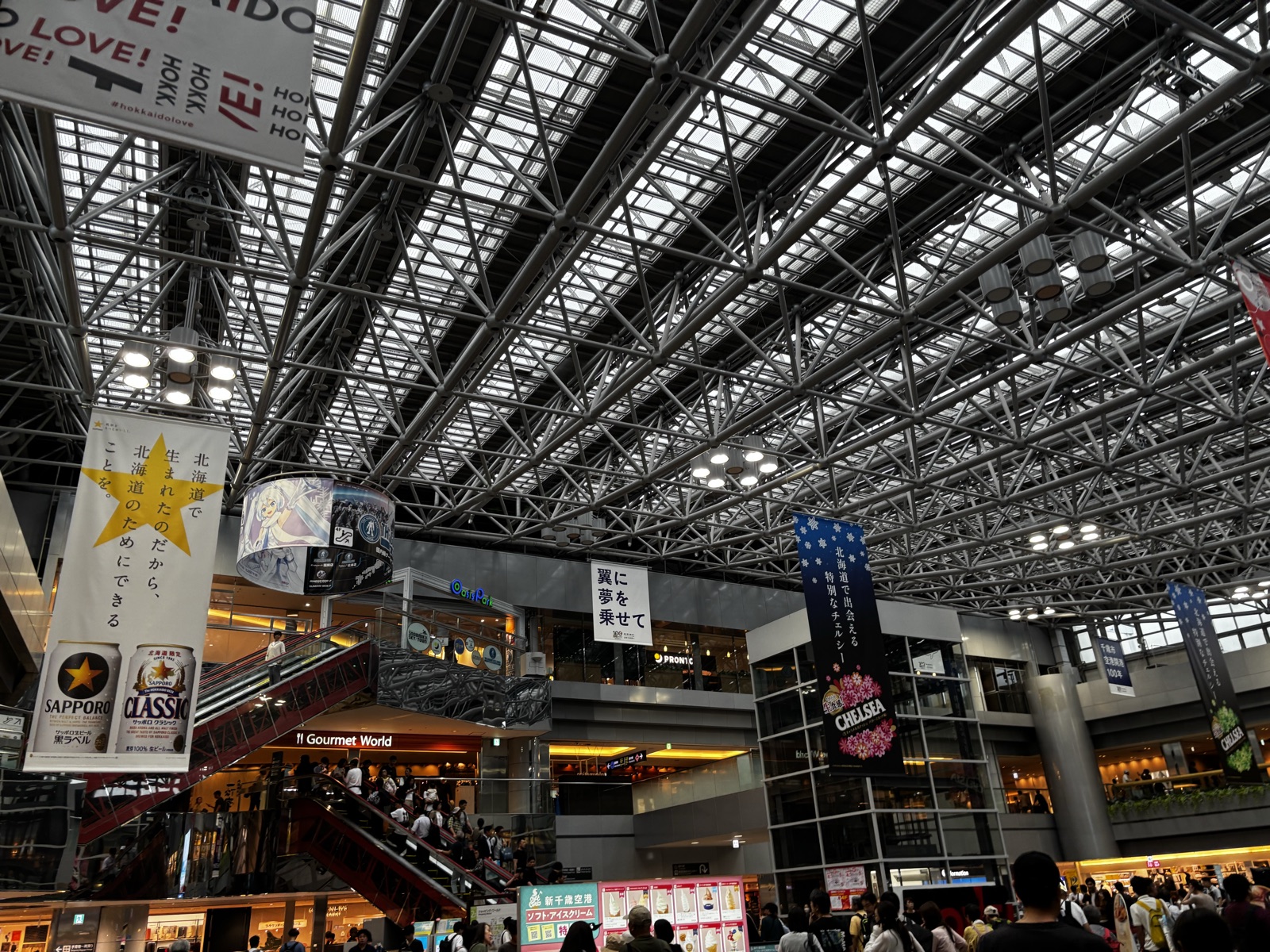 新千歳空港2階の吹き抜けの広場。3階グルメワールドへ上がる赤いエスカレーターとオアシス・パークの表示が見える